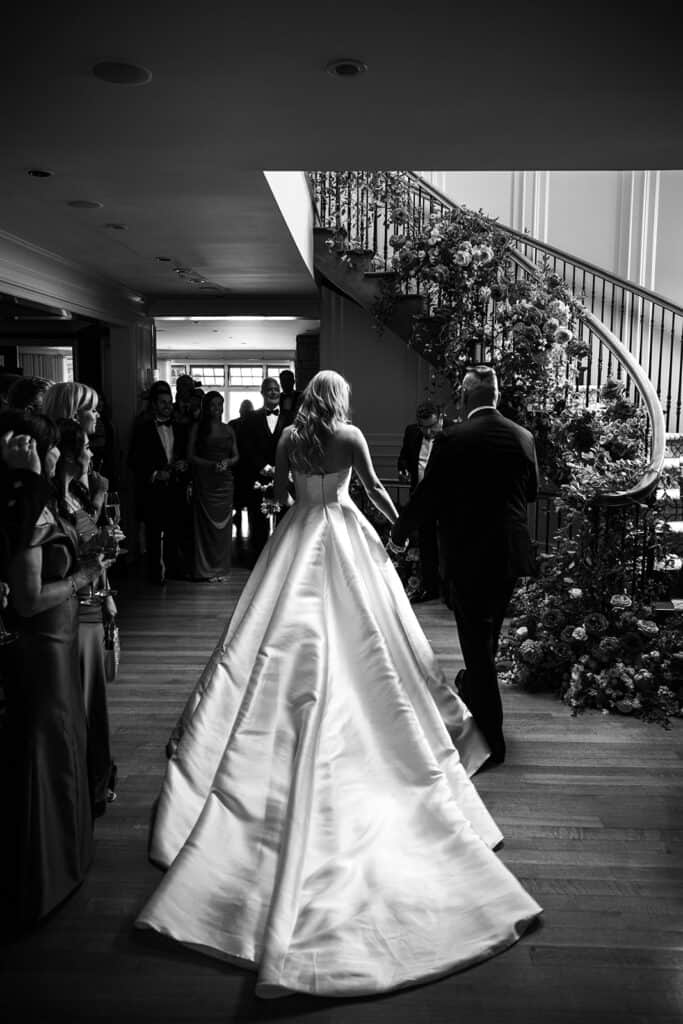 Black and white photography and rear view of the bride and groom walking down the aisle in at a wedding ceremony at home in Fredericton, NB